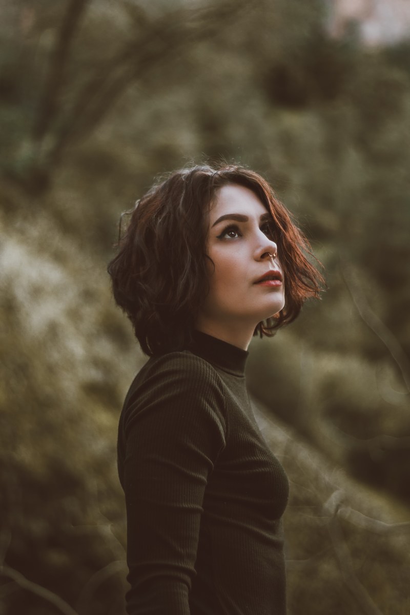 woman in a turtleneck looks up in the woods, wandering the woods 4k