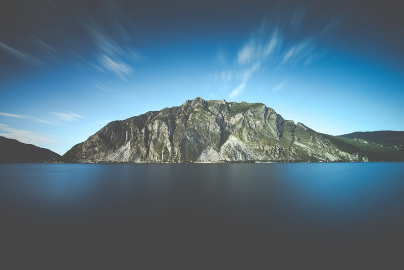 a rock mountain surrounding a body of water with moving clouds up in the sky, mountains near the water 4k
