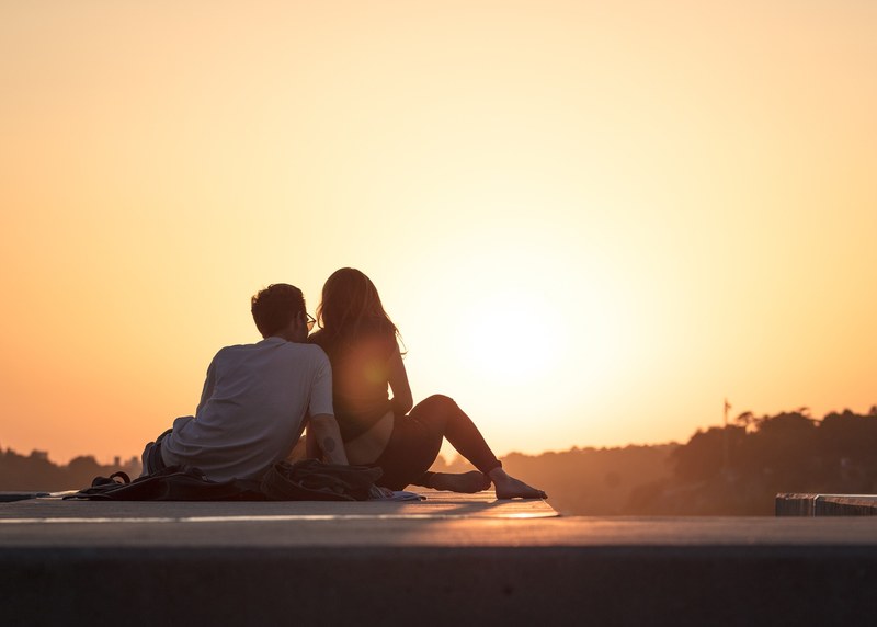 a couple sitting close together on a rooftop watching a golden sunset in esplanada do telefrico, love 4k
