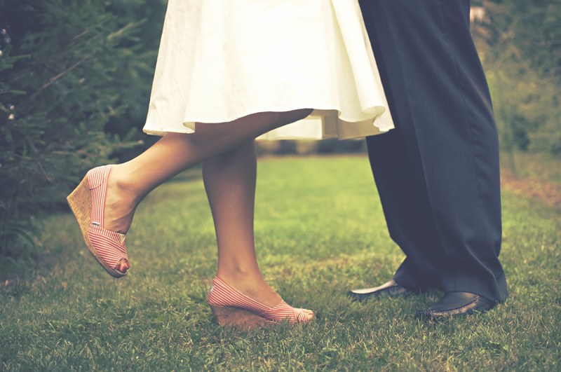 a bride and grooms legs in a short white dress and pink wedges and black suit, couple stands together on grass 4k