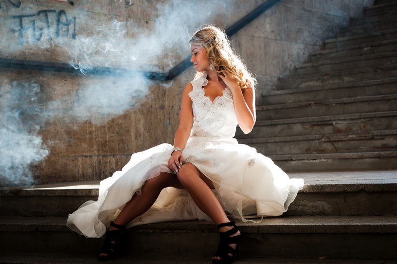 woman in a wedding gown siting on a smoky subway staircase, bride poses next to graffiti 4k