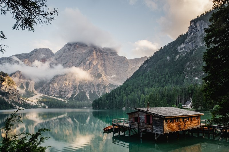 a log cabin lakehouse and dock on lago di braies with the snow capped mountains in the background, boathouse on a mountain lake 4k