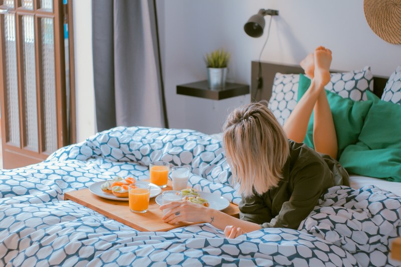 a woman laying on her bed eating breakfast on a blue and white bedspread in her bedroom in her apartment in barcelona, breakfast in bed 4k