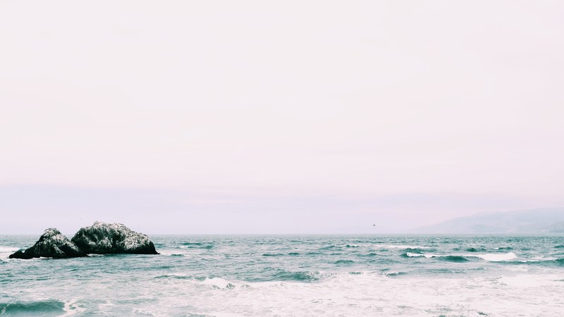 two weathered rocks jutting out from the rough blue sea, two rocks in blue sea 4k