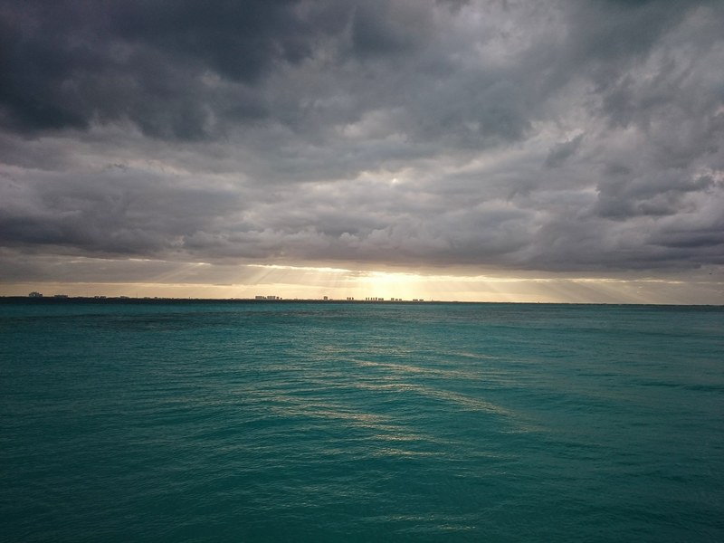 a turquoise sea with a city skyline on the horizon on a cloudy day, skyline by the sea on a cloudy day 4k