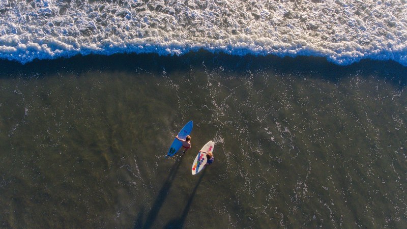 an overhead shot of a couple with surfboards walking into the sea, sean and seth 2 4k