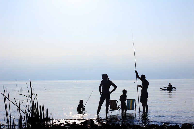 silhouettes of a family fishing by the sea of galilee and a man paddling in kayak, wavesless 4k