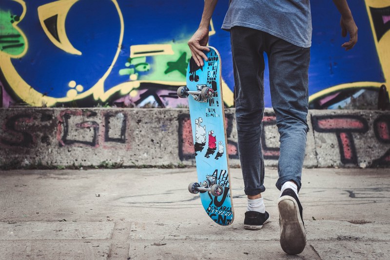 a person holds a decorated skateboard in front of a blue graffitied wall, person holding skateboard 4k