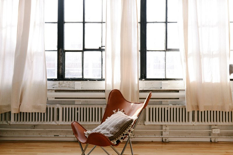 a brown leather chair with a throw pillow on it in a big light and airy room with white curtains in breather montreal, breather montreal interior 4k