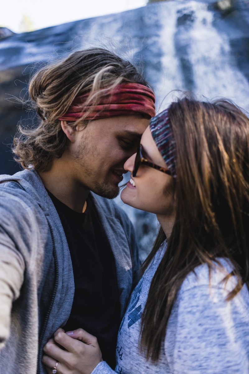 a rugged couple wearing headbands kisses in front of a waterfall in greenville, the moment after getting engaged 4k