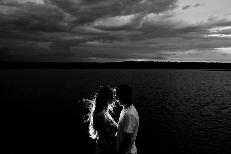 backlit couple in black and white photograph sharing an intimate moment at night on the water, in this moment illuminated 4k