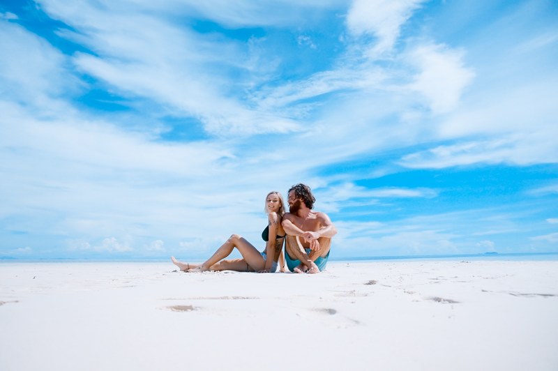 a couple sitting close to each other on a white sandy beach, young couple on an empty beach 4k