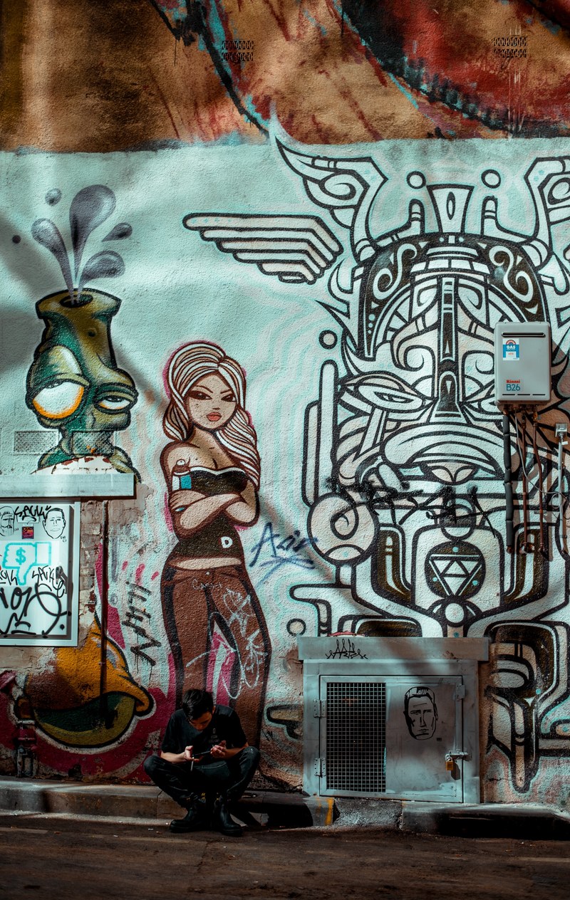 man sitting in front of detailed urban graffiti artwork in melbourne, street art walking in melbourne 4k