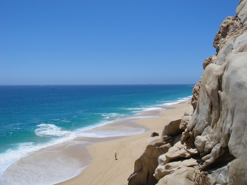 rock cliff overlooking a person standing on the sand beach coastline at mexico, cliff on a sandy coastline 4k
