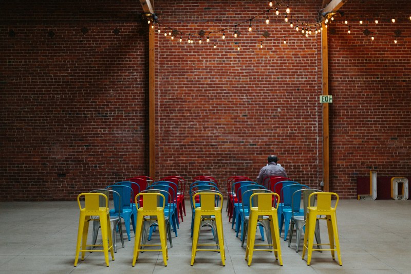 person sits alone in rows of colorful chairs inside a decorated event space, take a seat 4k