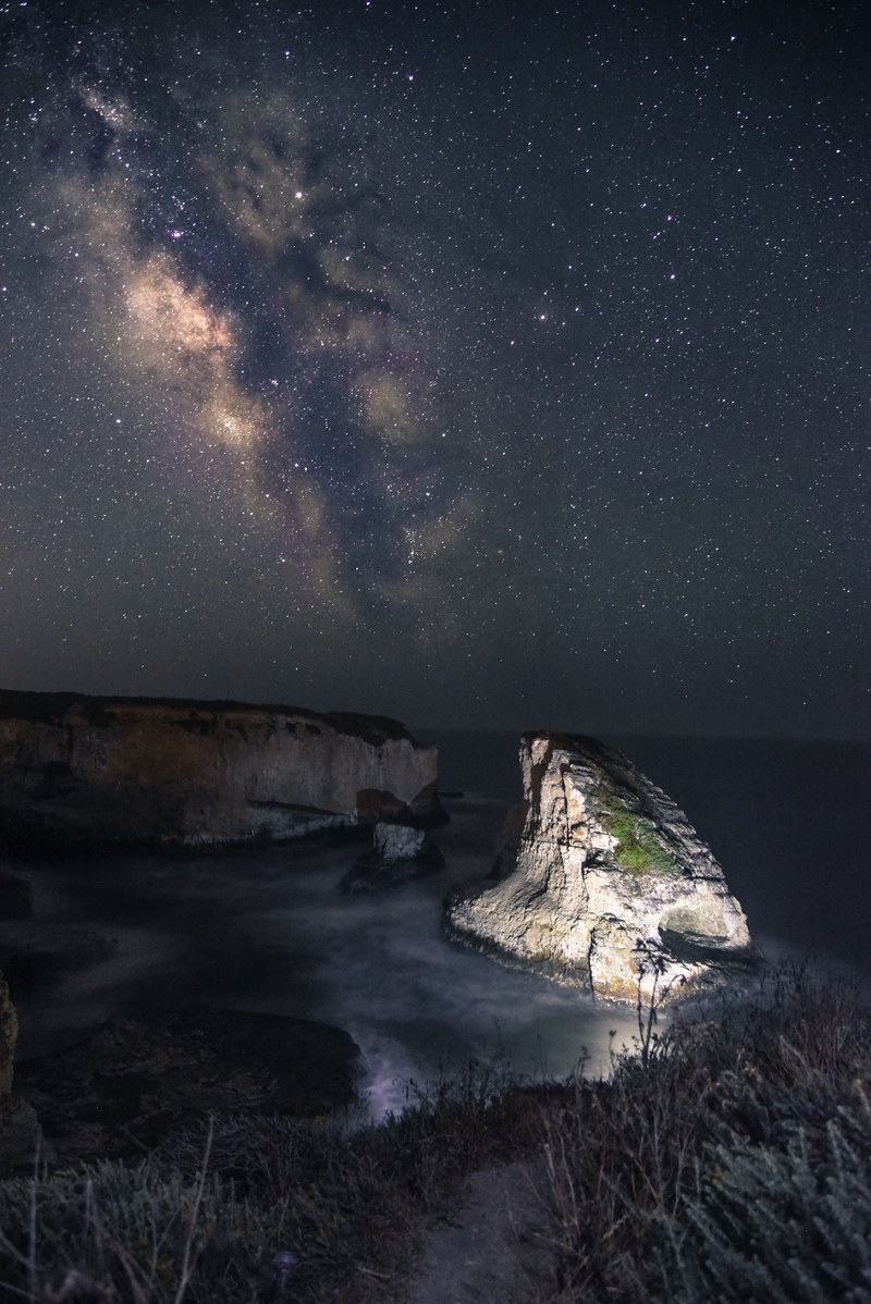 the milky way rises above the lighted up shark fin cove in the star studded night, _shark fin cove under the night sky 4k
