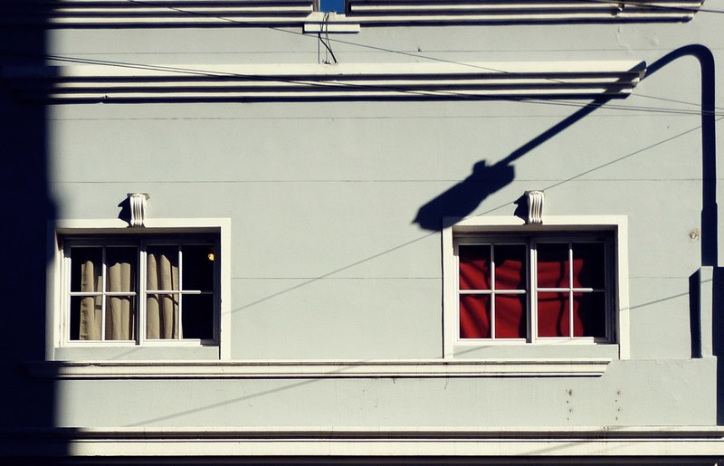 a long lamppost shadow on the wall of a building with two small windows, shadow on a facade 4k