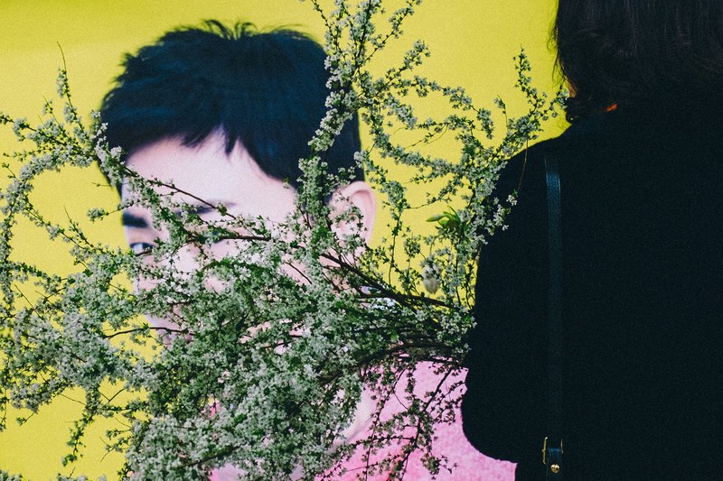 a woman carrying long branches with tiny white flowers in front of a wall with a mans face painted on it, woman with flowery branches 4k