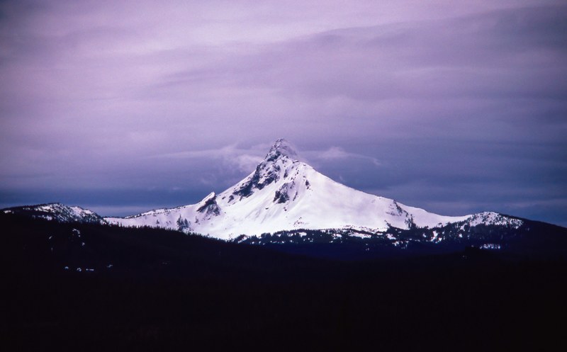 a tall mountain peak with a thick layer of snow on its sides on a cloudy day, tall peak under overcast sky 4k