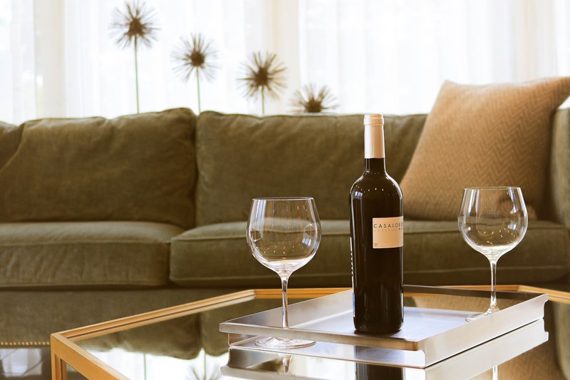 two wine glasses and a bottle of red wine on a glass table in a livingroom with a couch in the background, after work drink 4k