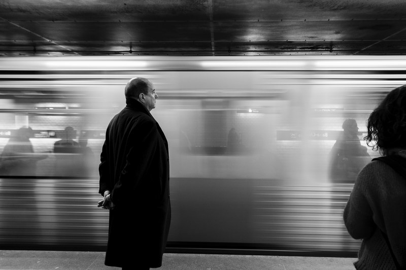 black and white shot of bald man standing in coat on subway platform with moving train, bald man on subway platform 4k