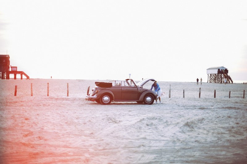 woman watching under the bonnet of vintage volkswagen beetle cabrio at the sand beach in sankt peter ording, driving on the beach 4k