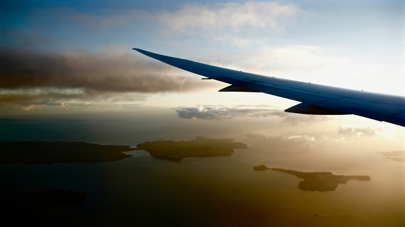 a view from the window of an airplane on its wing and green islands on the ocean below, in the air above green islands 4k