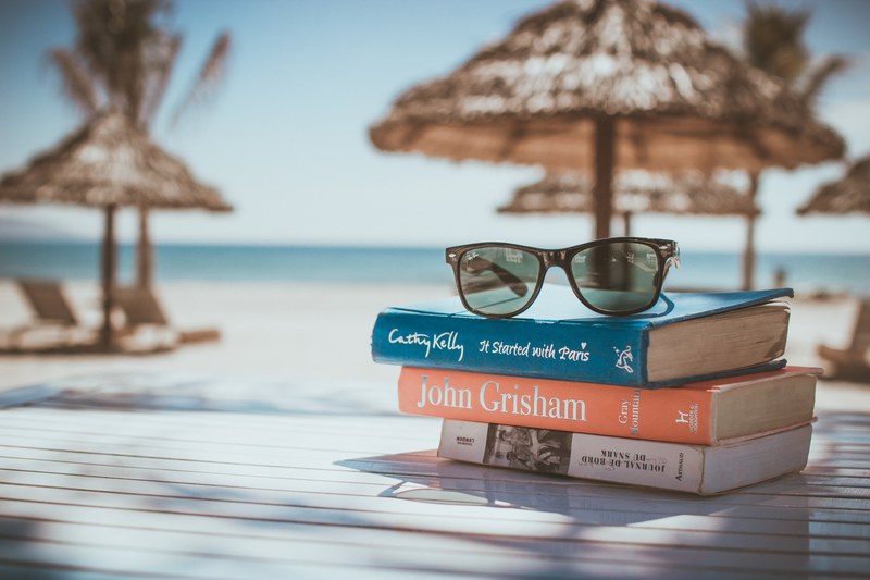 a pair of sunglasses is on top of books by famous authors on a beach table, _beach table da nang 4k