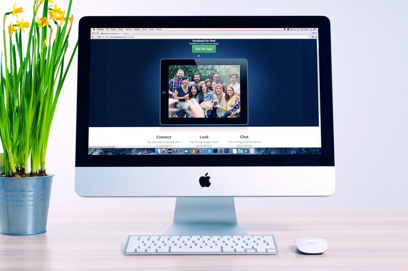 facebook site displayed on the screen of an imac next to potted daffodils, daffodils on a computer desk 4k