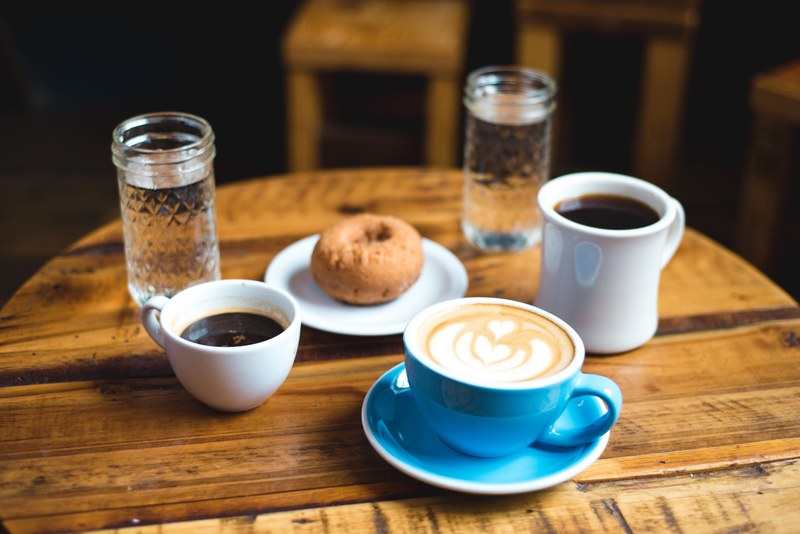 a round coffee table with two cups of black coffee a latte with an artwork a donut and water in glasses, coffee and a sweet snack 4k