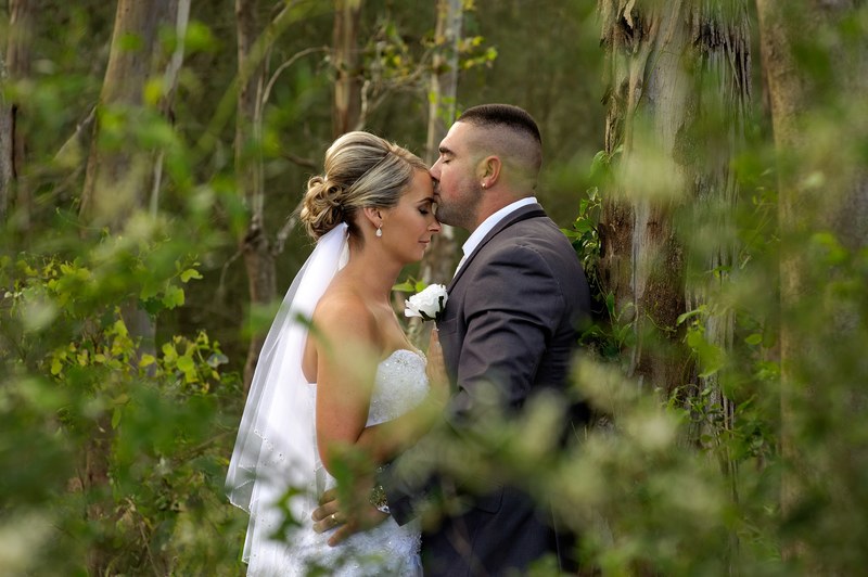 a man kisses a womans forehead in a forest of trees on their wedding day, groom gives bride forehead kiss 4k
