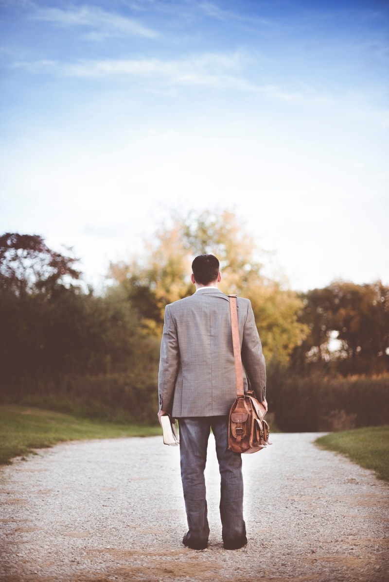 a man in a suit with a leather bag on his arm and a thick book in his hand on a dirt path, career path 4k