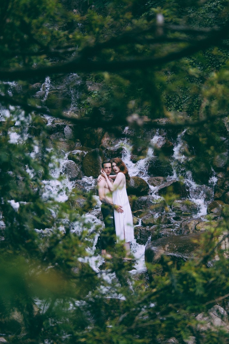 a shirtless man and a woman in a dress embrace near a waterfall in the woods, _young love 4k