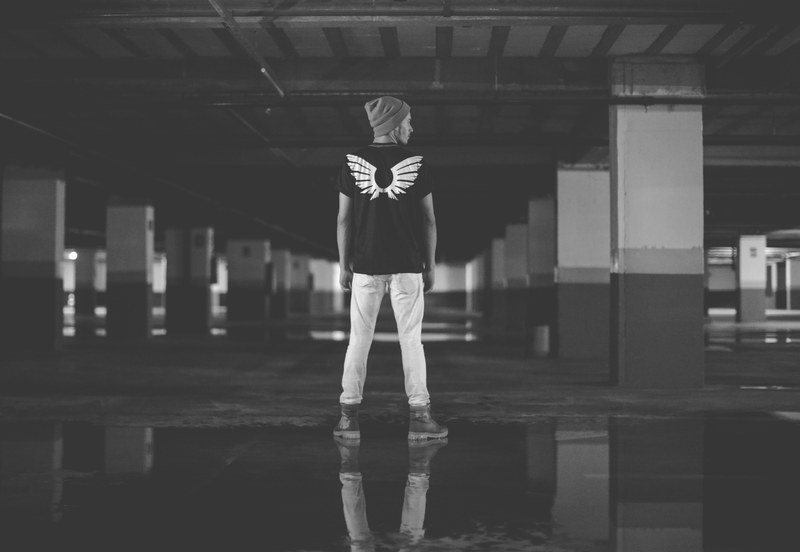 a man with wings on the back of his shirt looking in a parking garage, lost in parking garage 4k