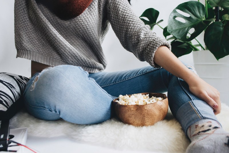 woman in a cropped gray sweater sits on a furry rug with a bowl of popcorn, textures unfolded 4k