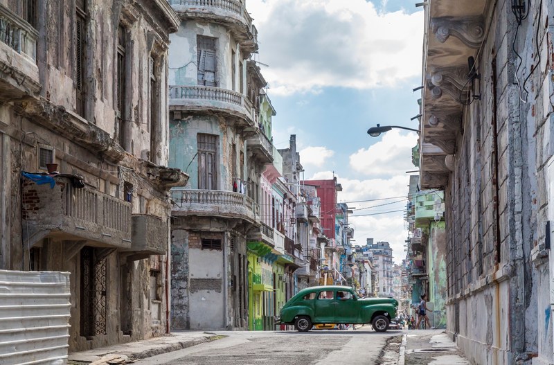 a vintage green car driving along dilapidated buildings, vintage car driving in centro havana 4k