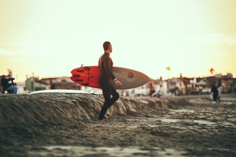surfer in wetsuit with a surfboard on a sandy beach at 54th street, surfer in wetsuit 4k