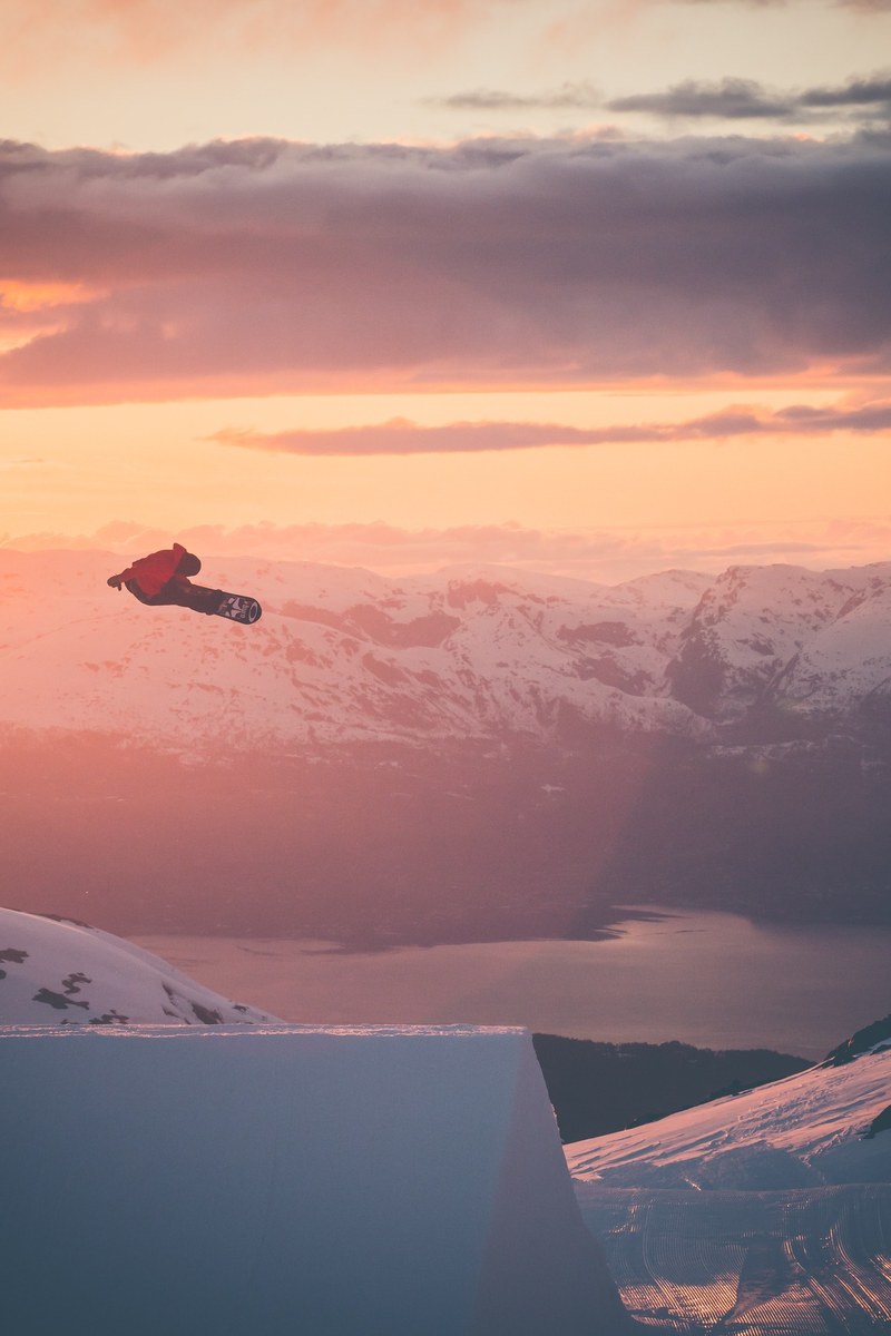 a snowboarder is airborne surrounded by golden skies and snowy mountains, snowboarder in flight 4k