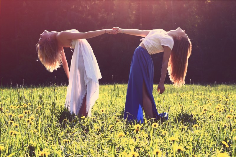 two women in dresses arching back while holding each other hands in a green meadow, two women in a meadow 4k