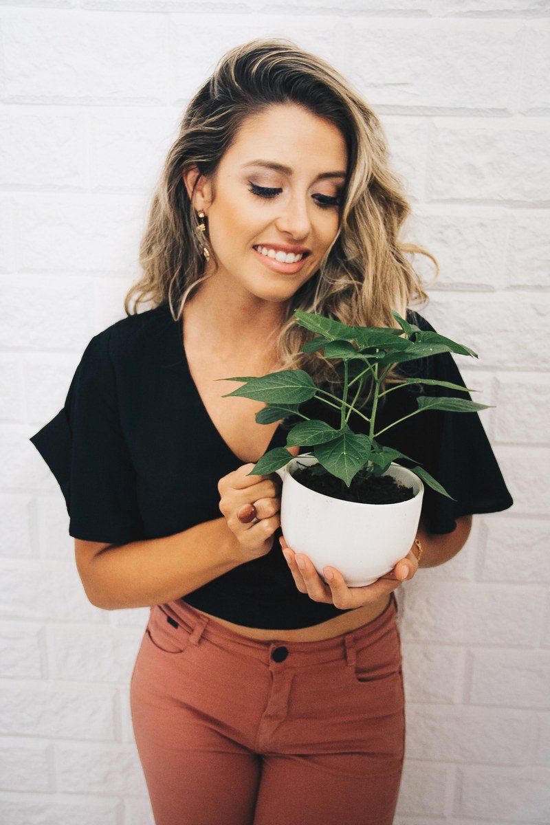 a smiling woman in a black t shirt and red jeans holds a potted plant, woman holding potted plant 4k