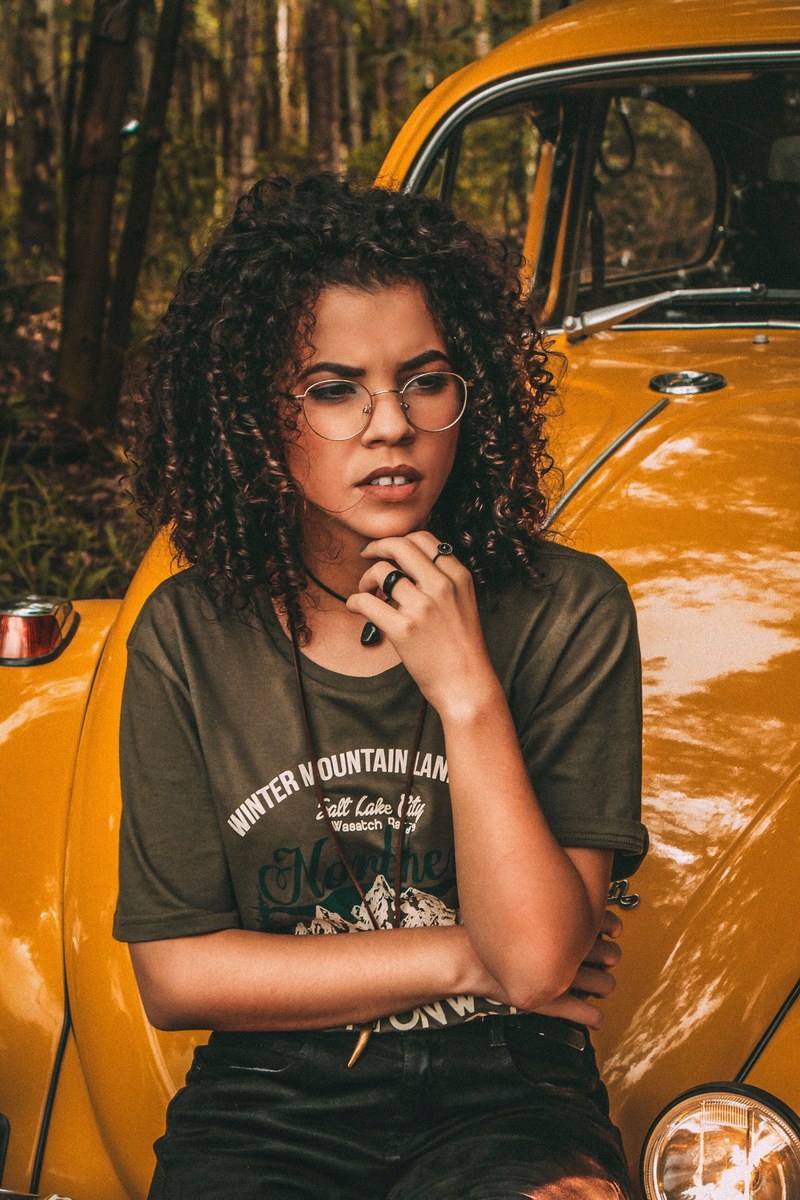 a young woman in glasses seated on the hood of a yellow volkswagen beetle, adventure explore 4k