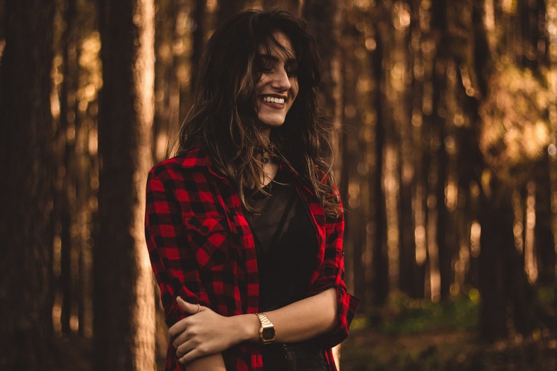 brown haired woman wearing a plaid red and black jacket and a watch in the forest, golden sunlit forest 4k