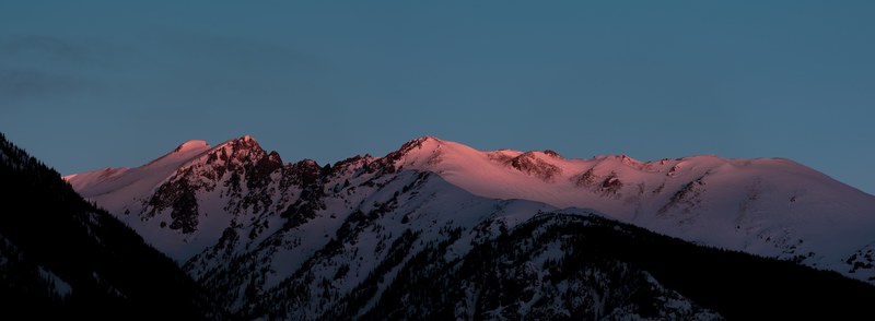 red light falls on the crest of a snow topped mountain during sunset, red sunset on a mountain 4k