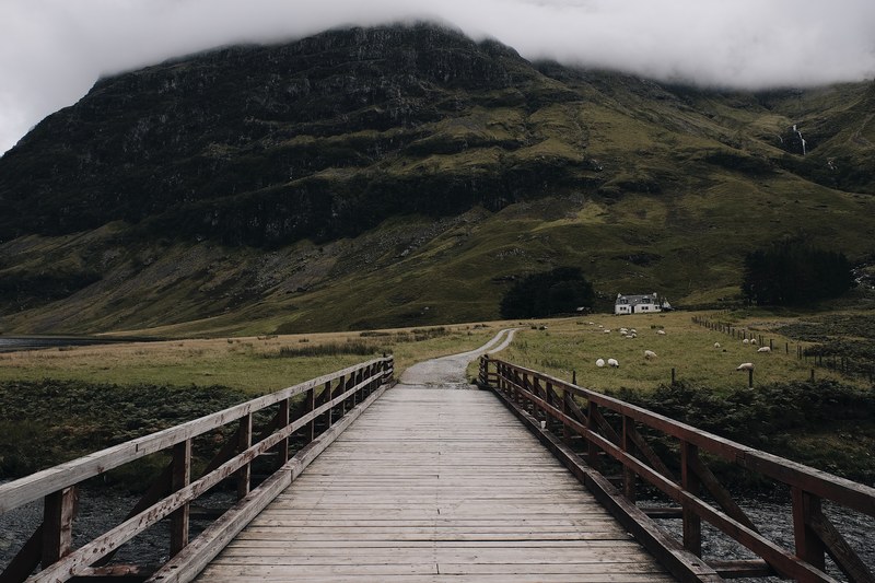 a boardwalk bridge crossing over to a trail near a grassy mountain, _a scottish landscape 4k