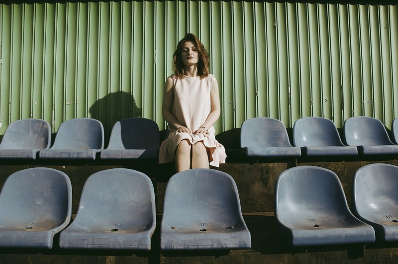 a woman in a dress sits in a row of chairs before a green wall, woman sitting in row of chairs 4k