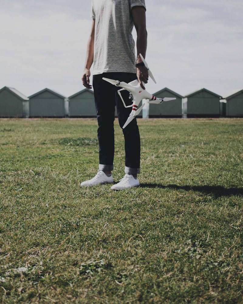 person in black pants holds a drone and remote in a grassy field, person holds drone 4k