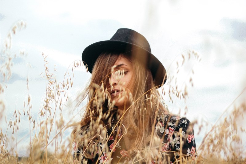 woman with a black hat standing behind grains of wheat, standing among wheat 4k