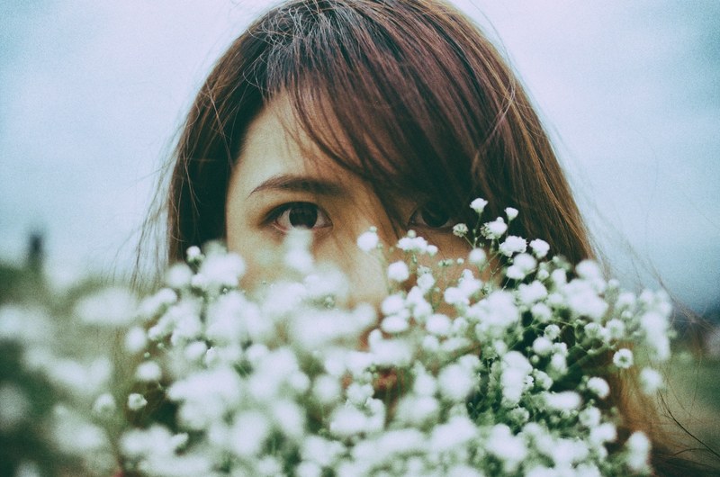a dark haired womans face behind a bunch of tiny white flowers, deep eyes 4k