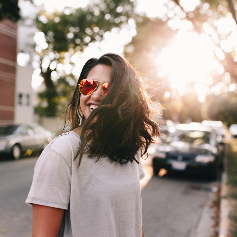 a smiling woman in sunglasses and a t shirt stands on a sunny street in chicago, fall is here 4k