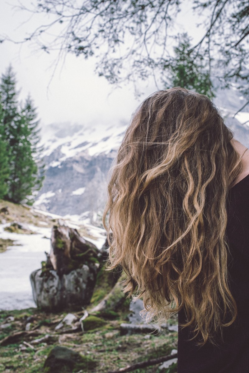 curly hair covers a womans face in a mountain landscape, wind through her hair 4k